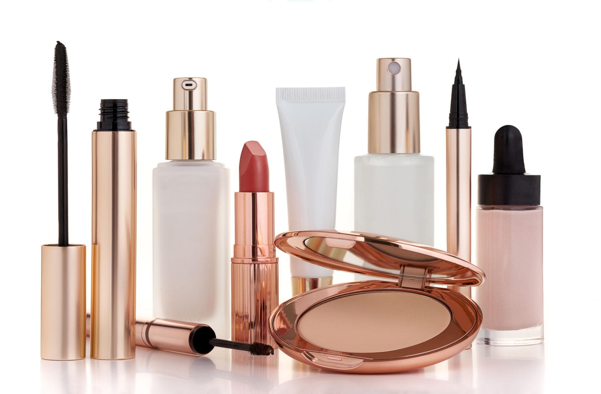 Mascara, lipstick, foundation, compact powder, and eyeliner lined up on a white background