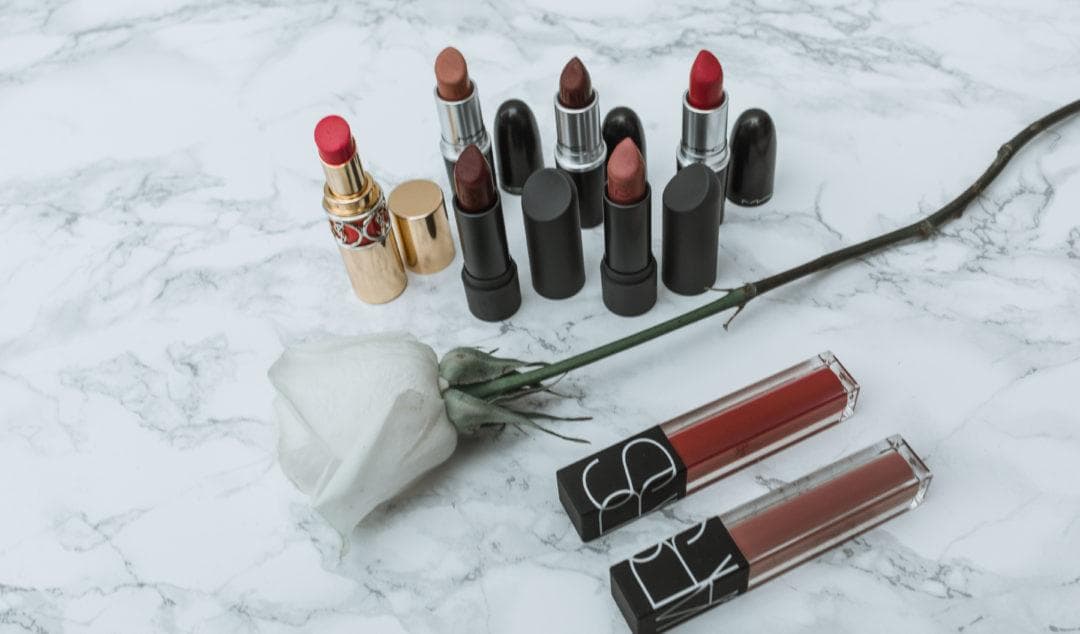 Lipsticks and lip gloss arranged on marble with a white rose